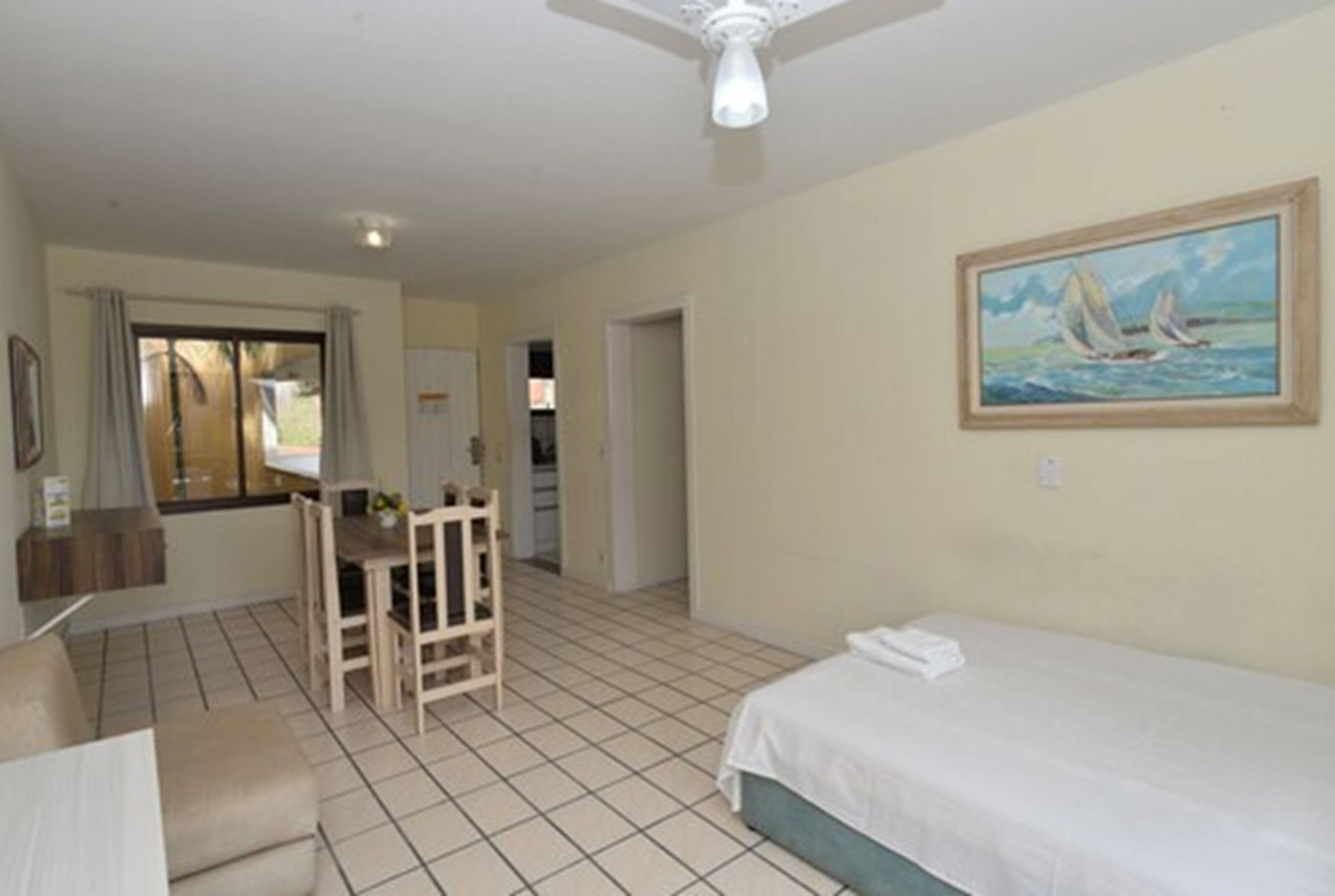 A hotel room with a bed, a desk, a chair, and a painting on the wall.