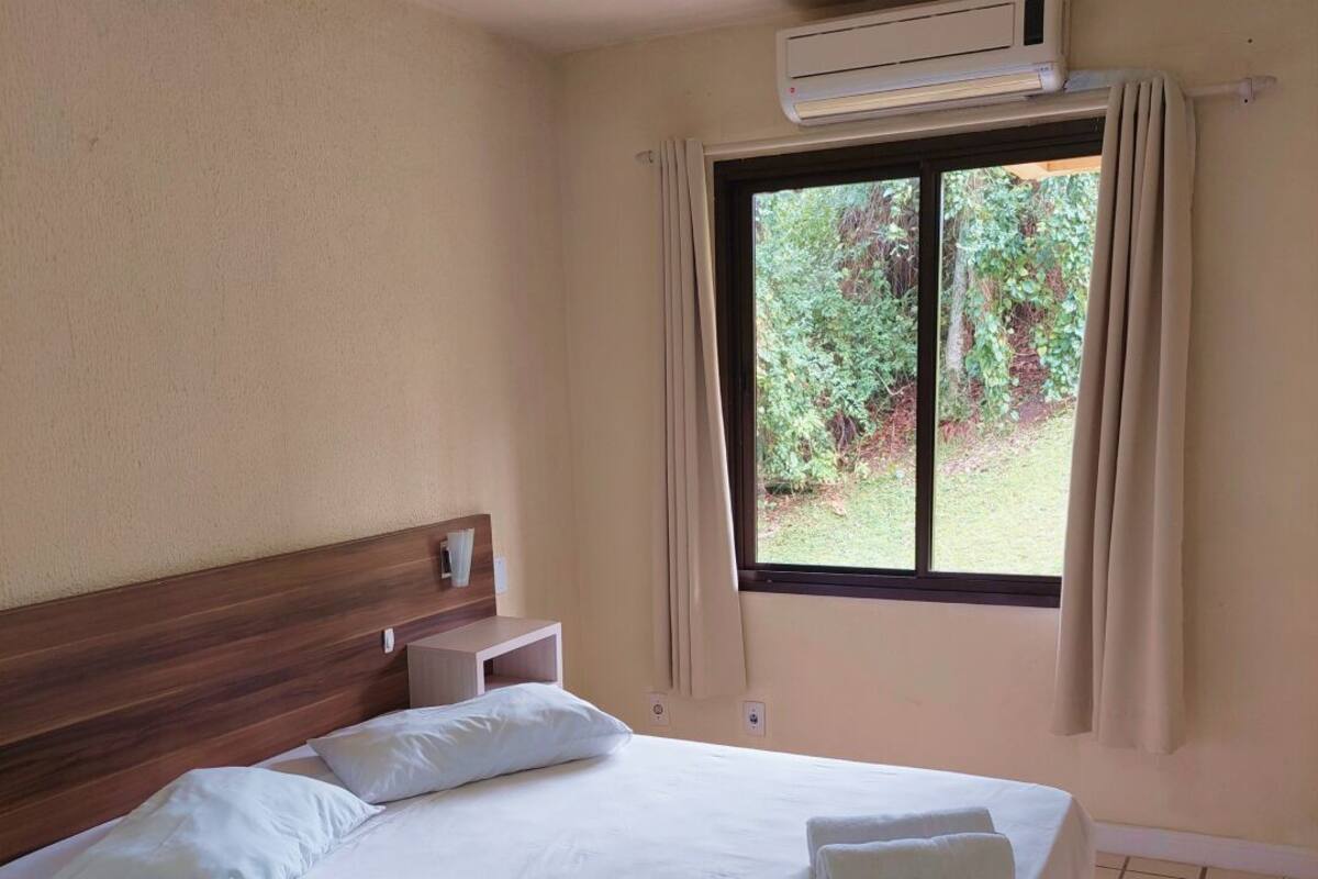 Une chambre d’hôtel équipée d’un lit, d’une table de chevet, d’un appareil de climatisation et d’une fenêtre avec des rideaux.