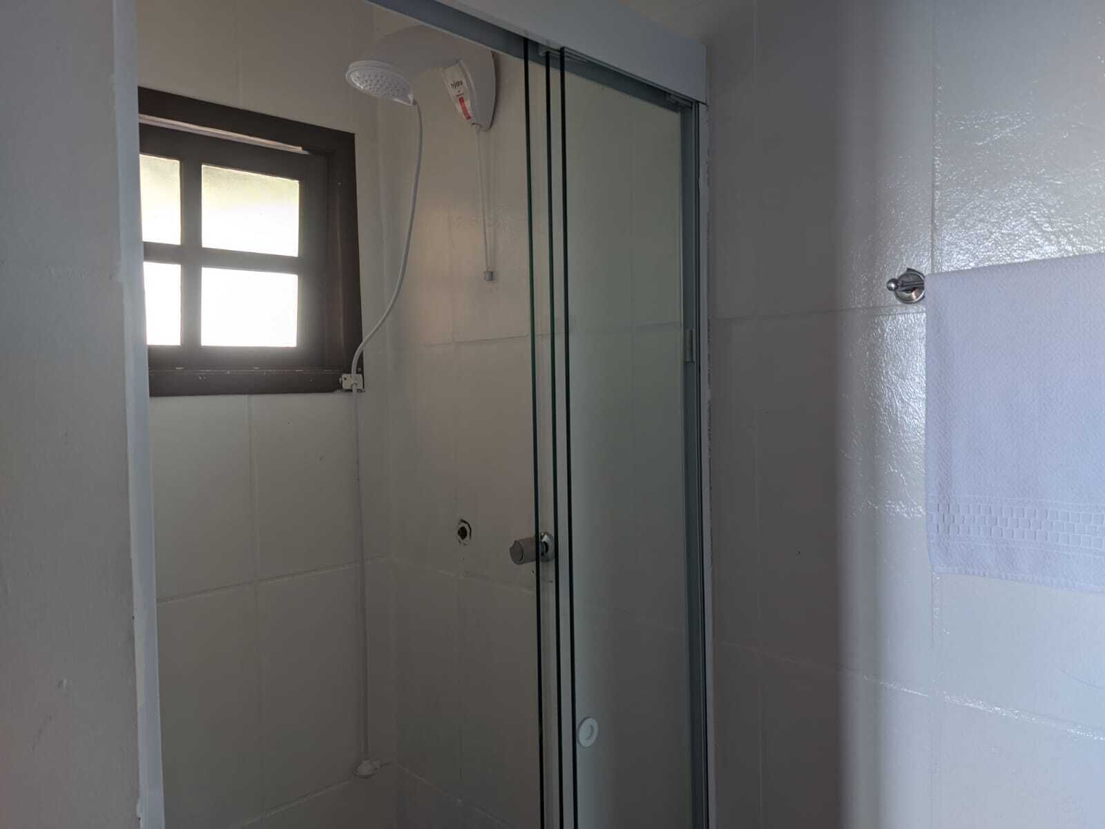 A glass-enclosed shower with a window, white tiled walls, and a door with a handle.