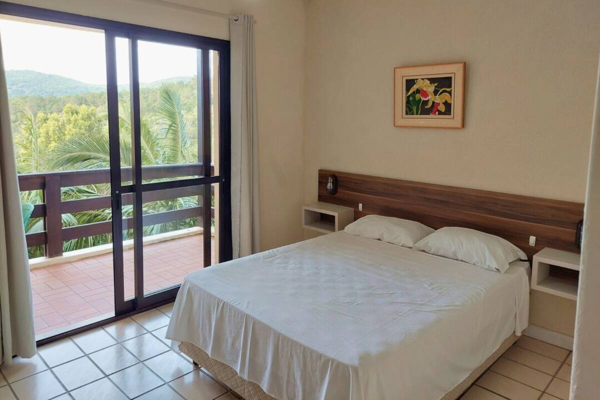 Une chambre d’hôtel avec un lit, une table de chevet, un tableau et une vue sur la verdure, visible à travers une porte coulissante.