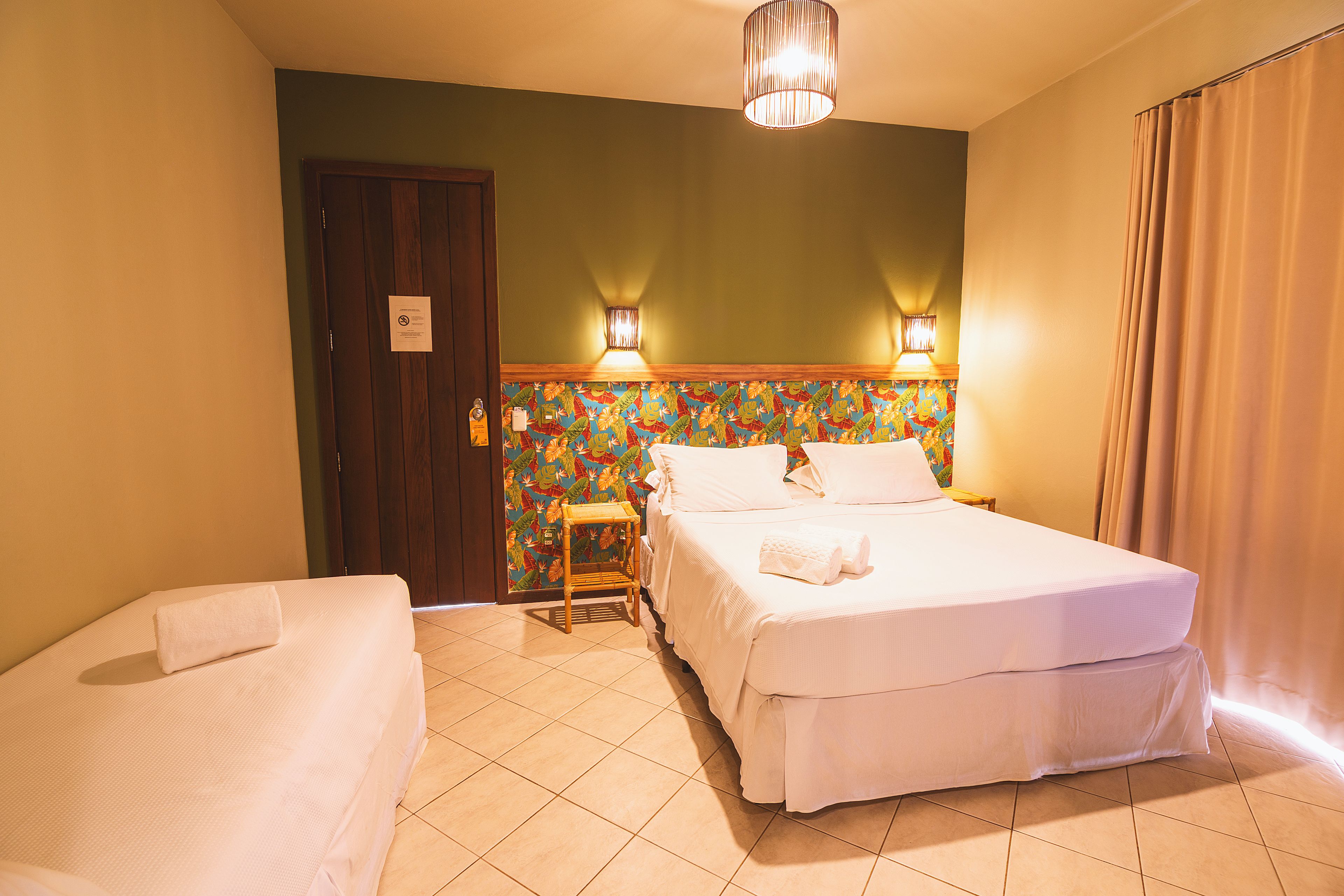 A hotel room with a bed, a chair, a door, and a wall with a floral pattern.