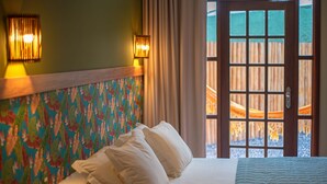 Hotelkamer met een bed, een kleurrijk hoofdbord en uitzicht op een houten terras door een glazen deur.