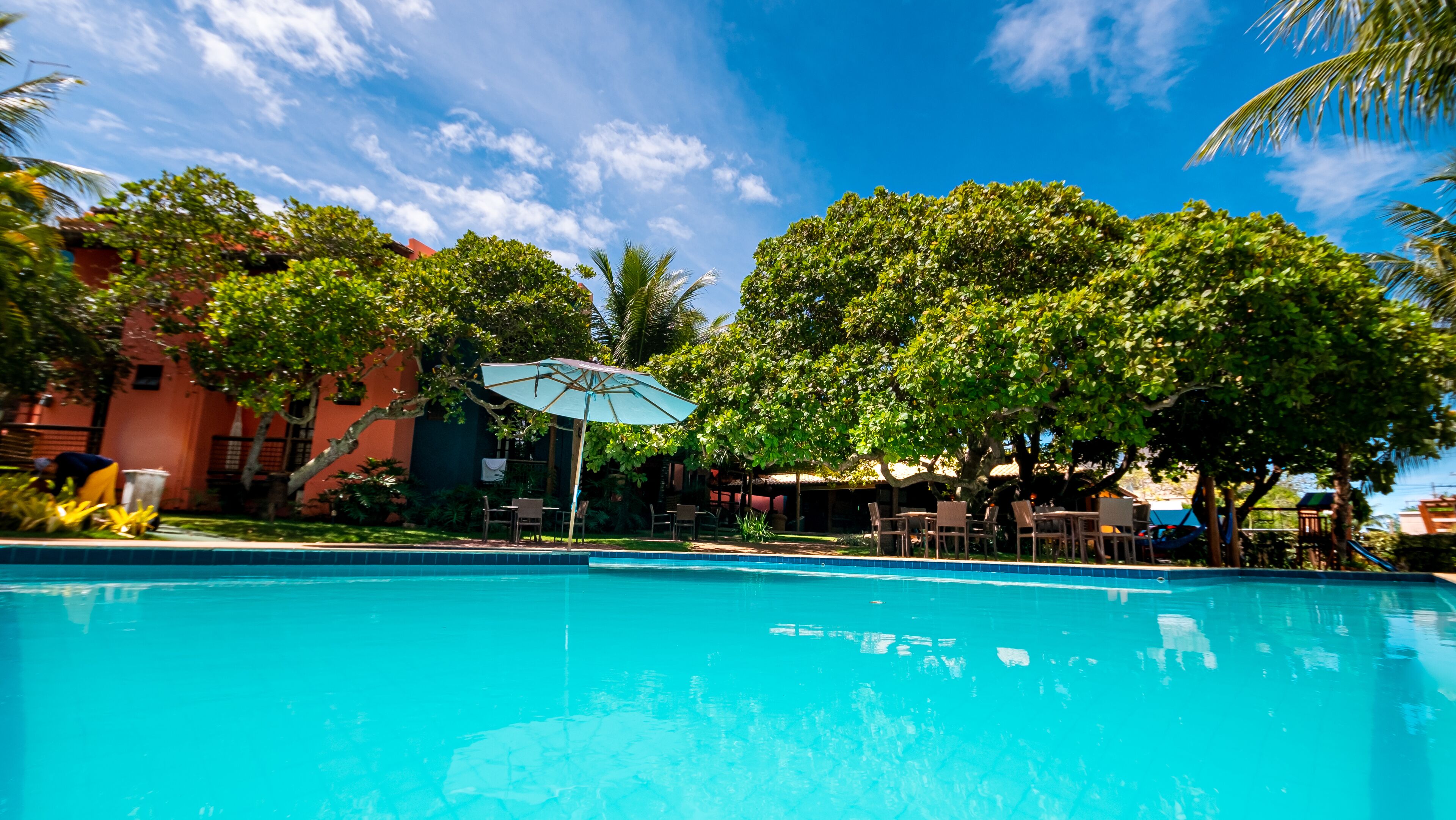 A swimming pool with lounge chairs and umbrellas, surrounded by lush greenery and a clear blue sky.