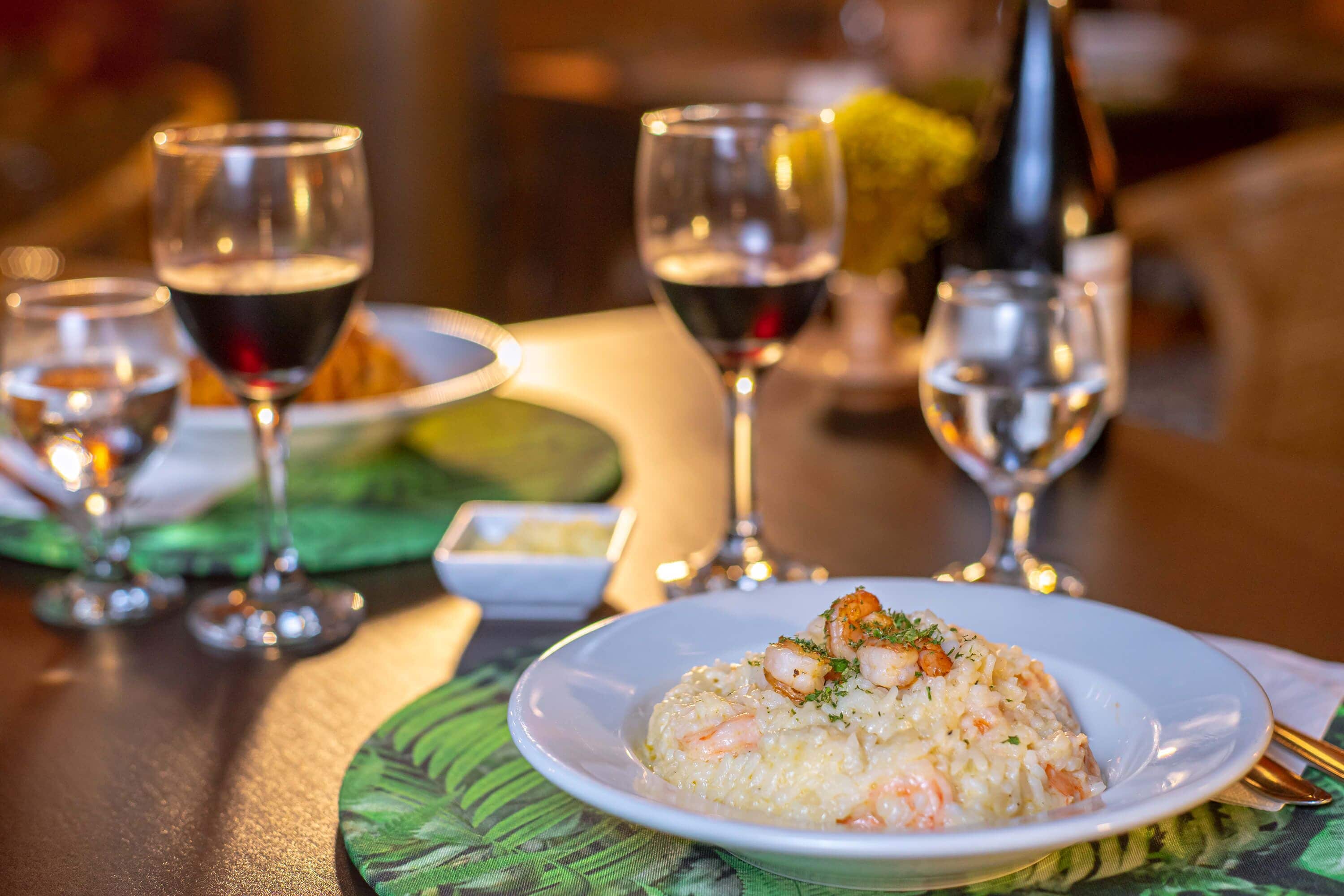 Une table à manger avec une assiette de risotto aux fruits de mer, des verres à vin et une bouteille de vin.