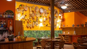 Een restaurantinterieur met een bar, rieten stoelen en een muur versierd met verschillende hoeden en flessen.