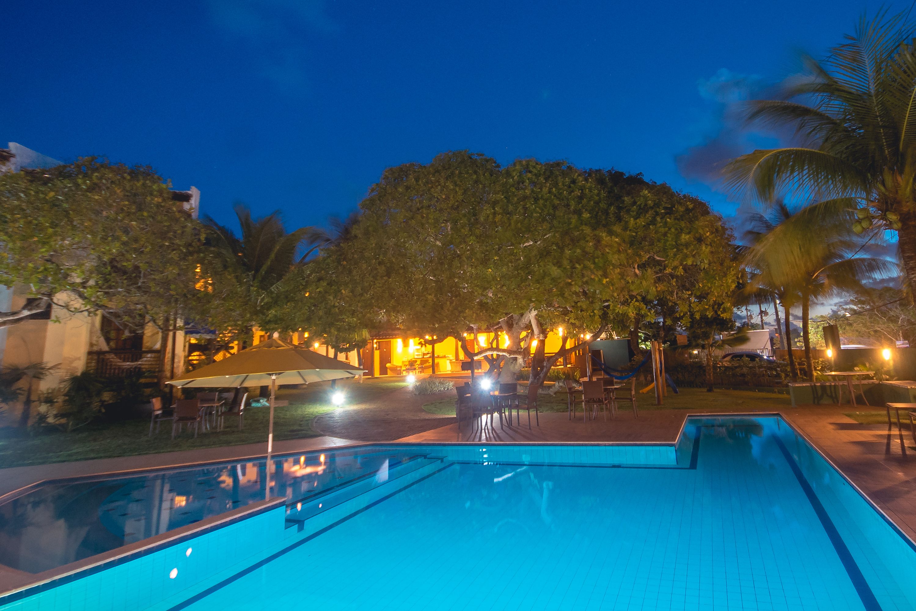 A swimming pool with a tiled deck, surrounded by palm trees and outdoor seating.