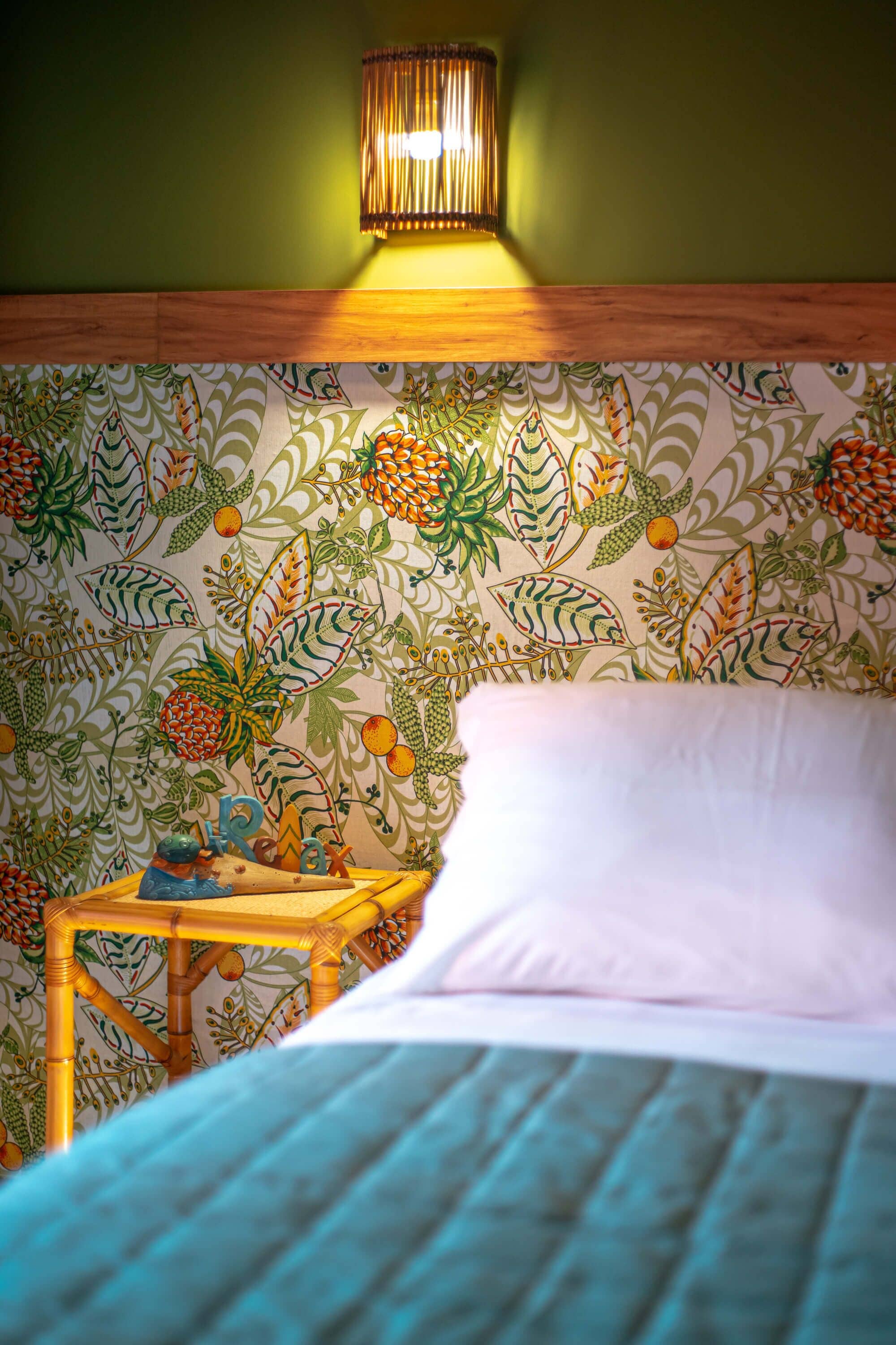 Una habitación con una cama, una mesita de noche con una lámpara y un papel tapiz con motivos florales.