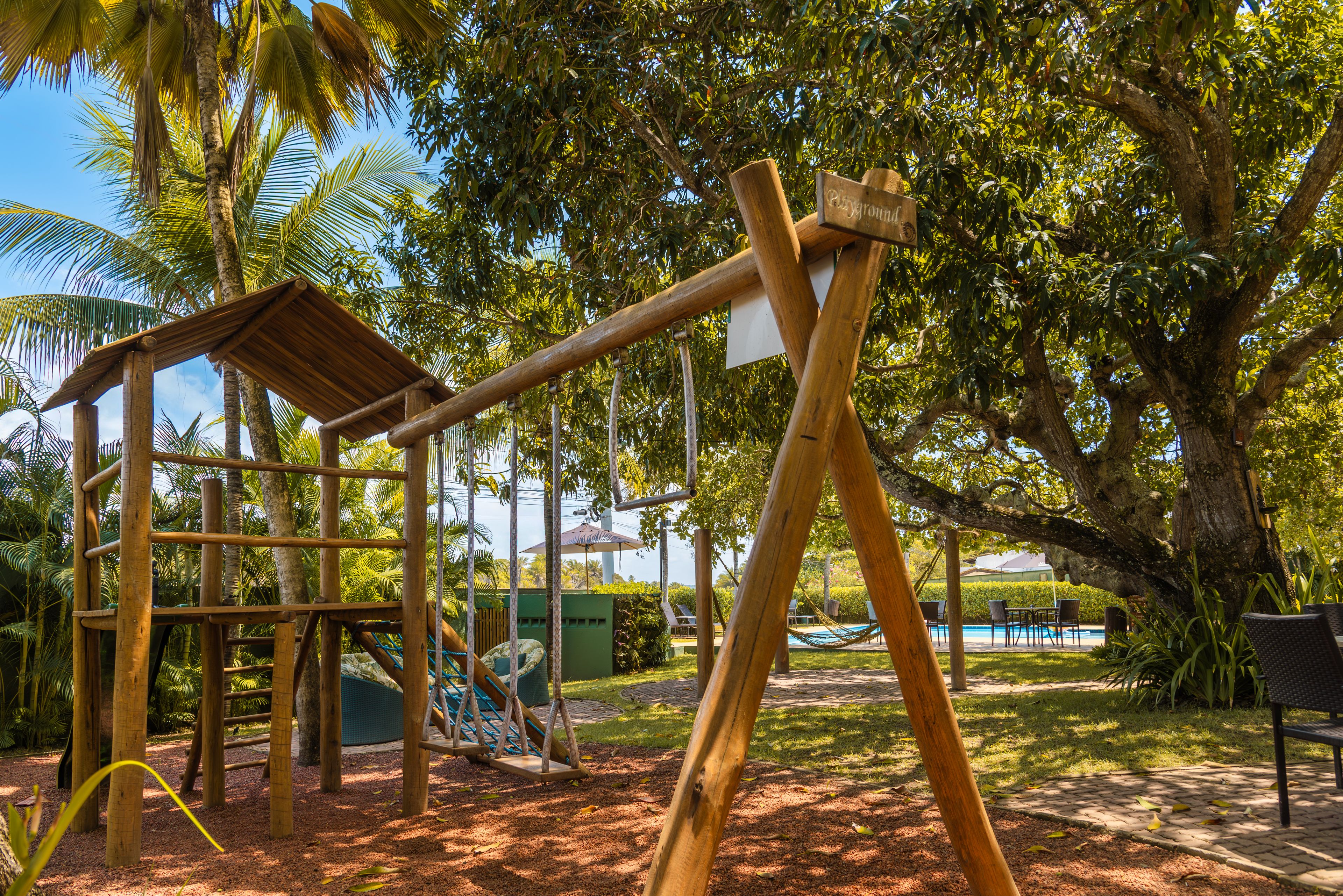 A playground with swings and a slide, surrounded by trees and a pool area.