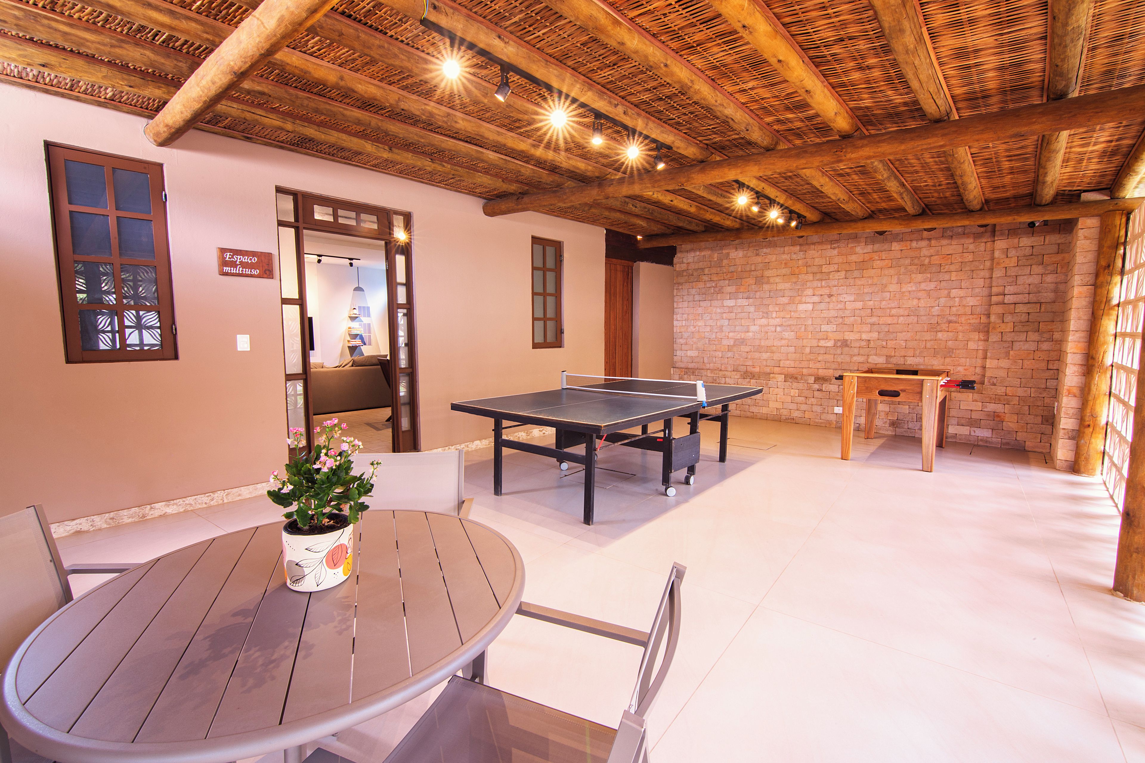 Una habitación con una mesa de ping pong, una mesa redonda con sillas y una pared de ladrillo.