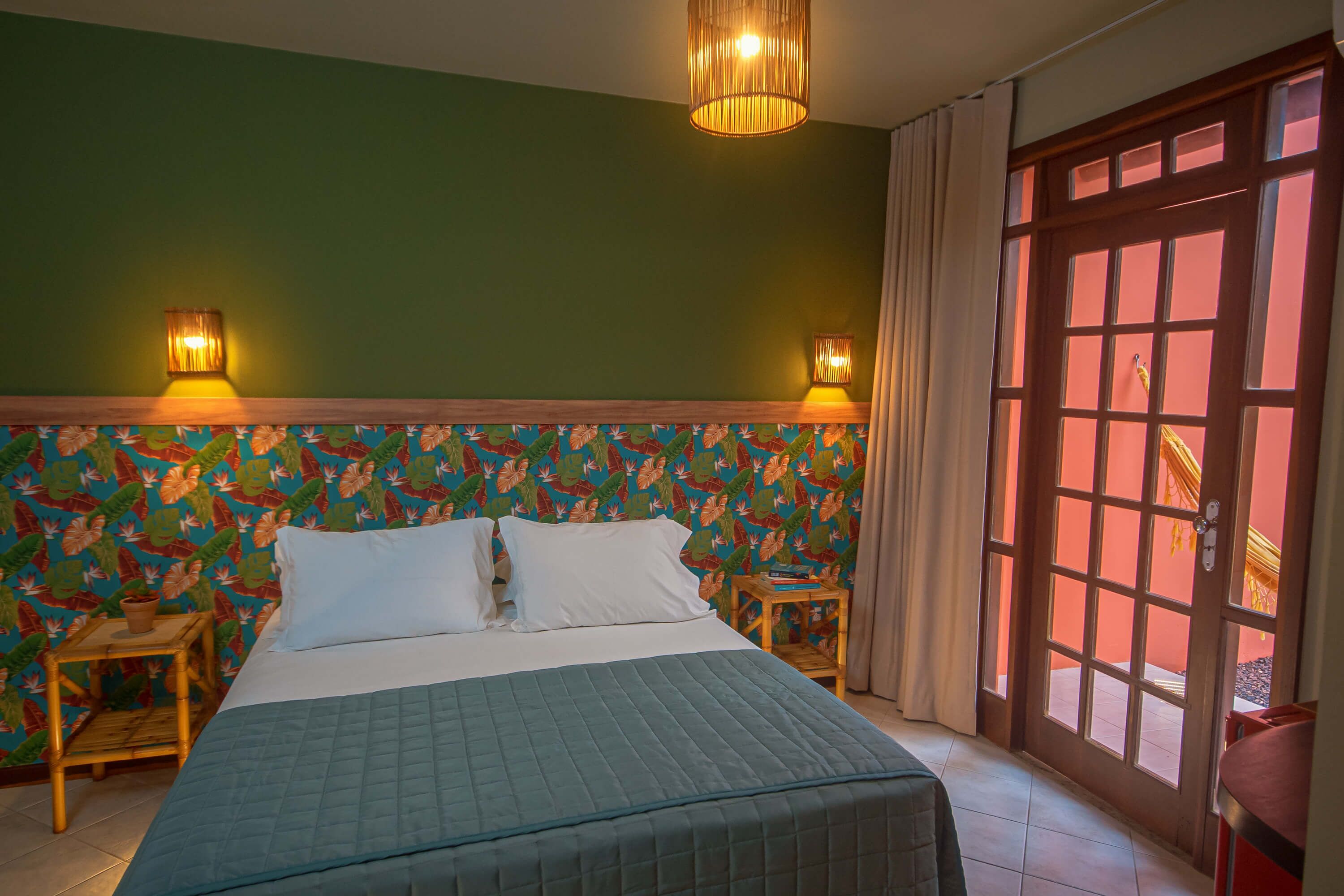 Een slaapkamer met een bed, twee bedlampen, een raam met gordijnen en kleurrijke bloemenbehang.