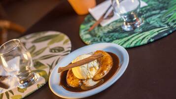 A dessert plate with a banana, ice cream, and a cinnamon stick on a table with a placemat.