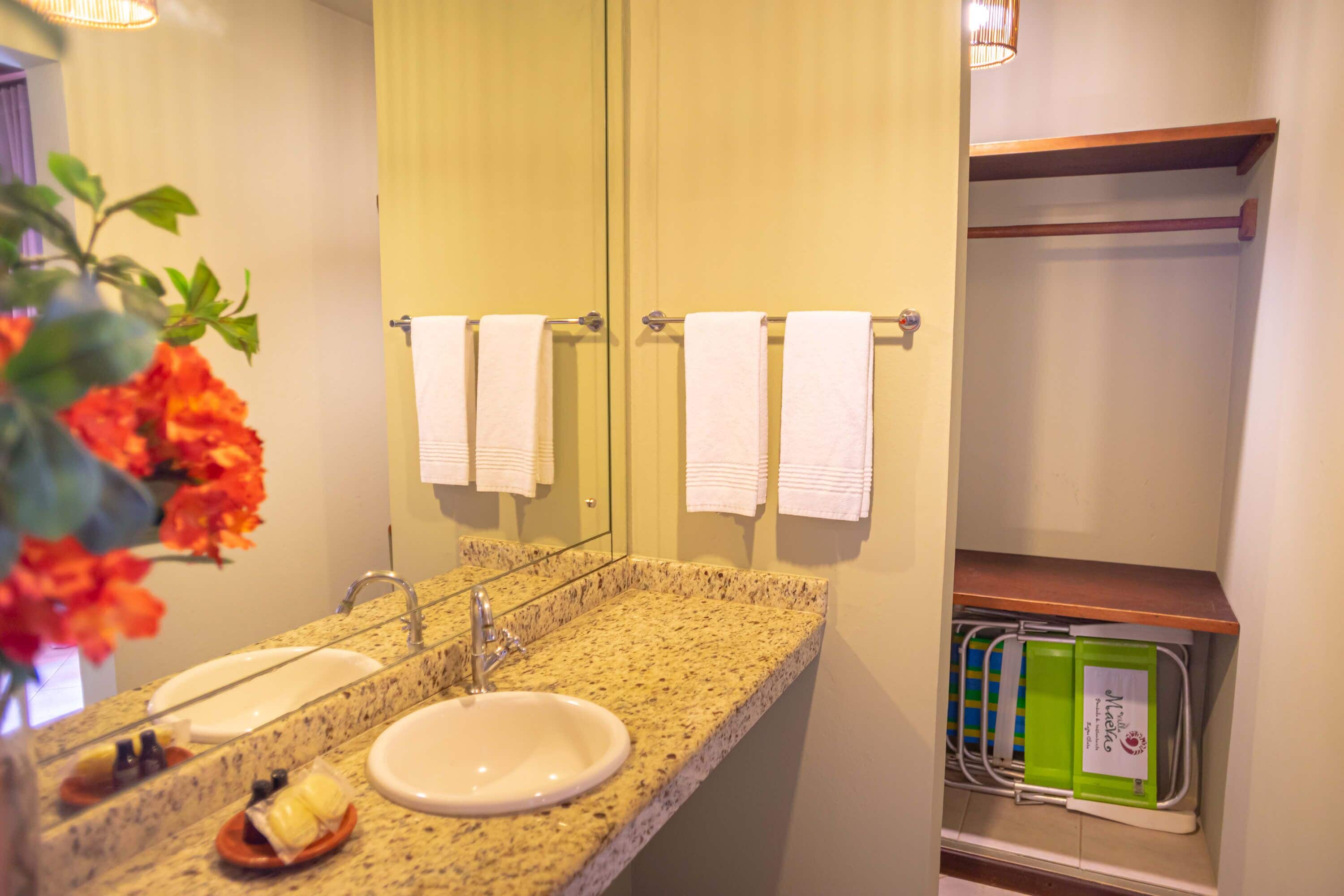 A bathroom with a granite countertop, two sinks, and a mirror. There are towels hanging on a rack and a green tray with a white towel.