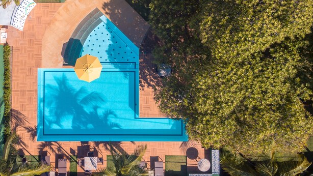 Luchtbeeld van een resort met een groot zwembad, palmbomen en een betegeld terras.