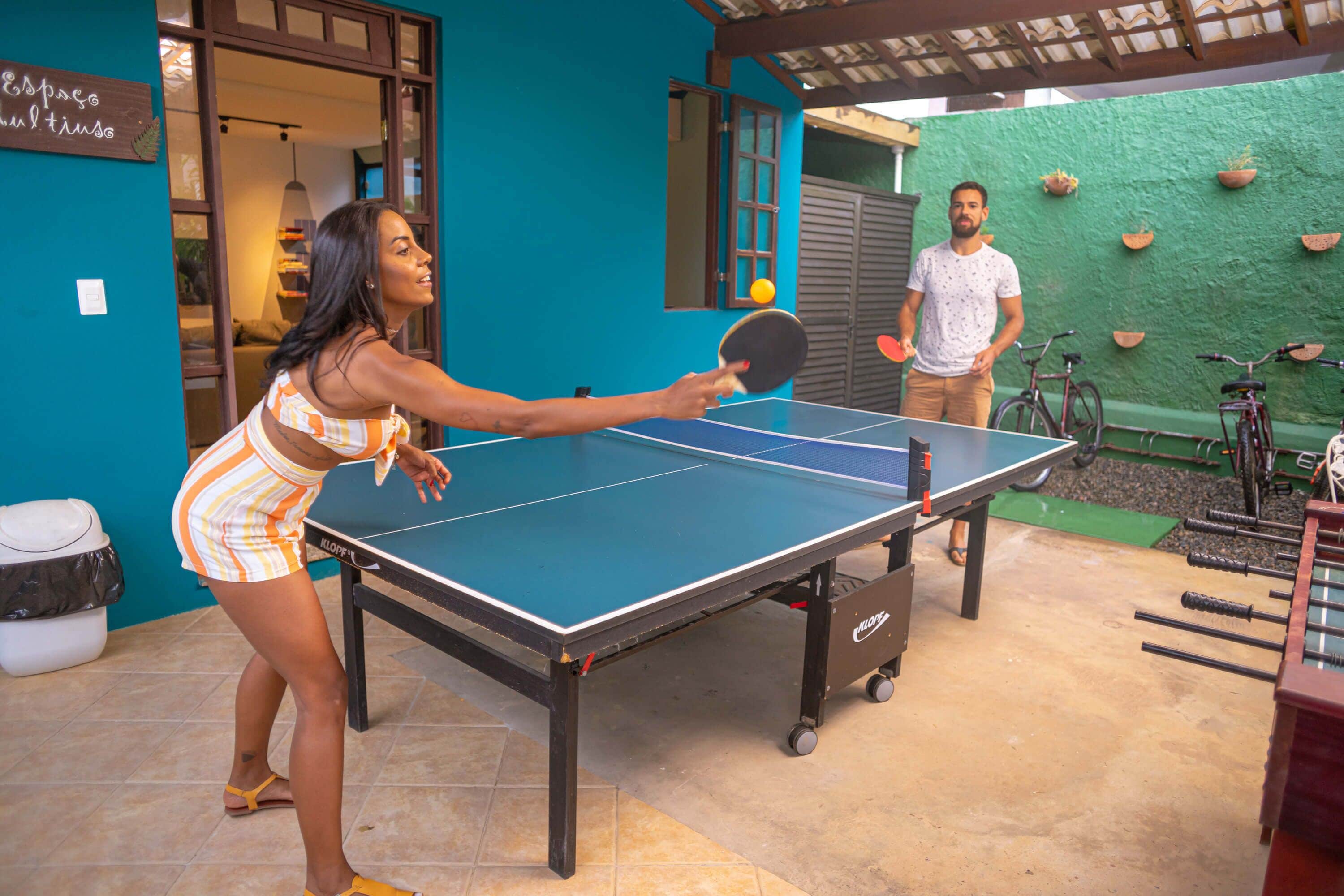 A ping pong table in an outdoor setting with a green wall and a bicycle in the background.