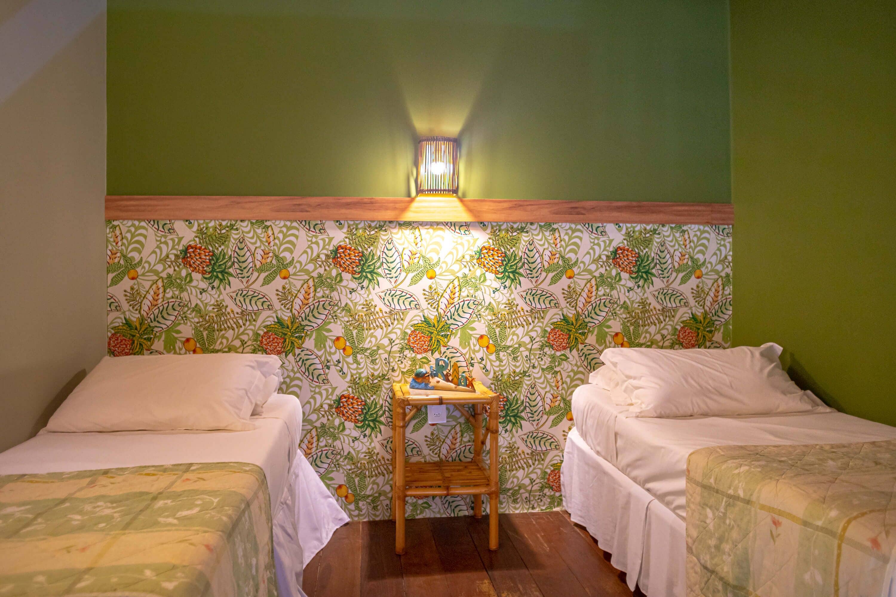 A room with two beds, a wooden nightstand, and a wall with a fruit pattern.
