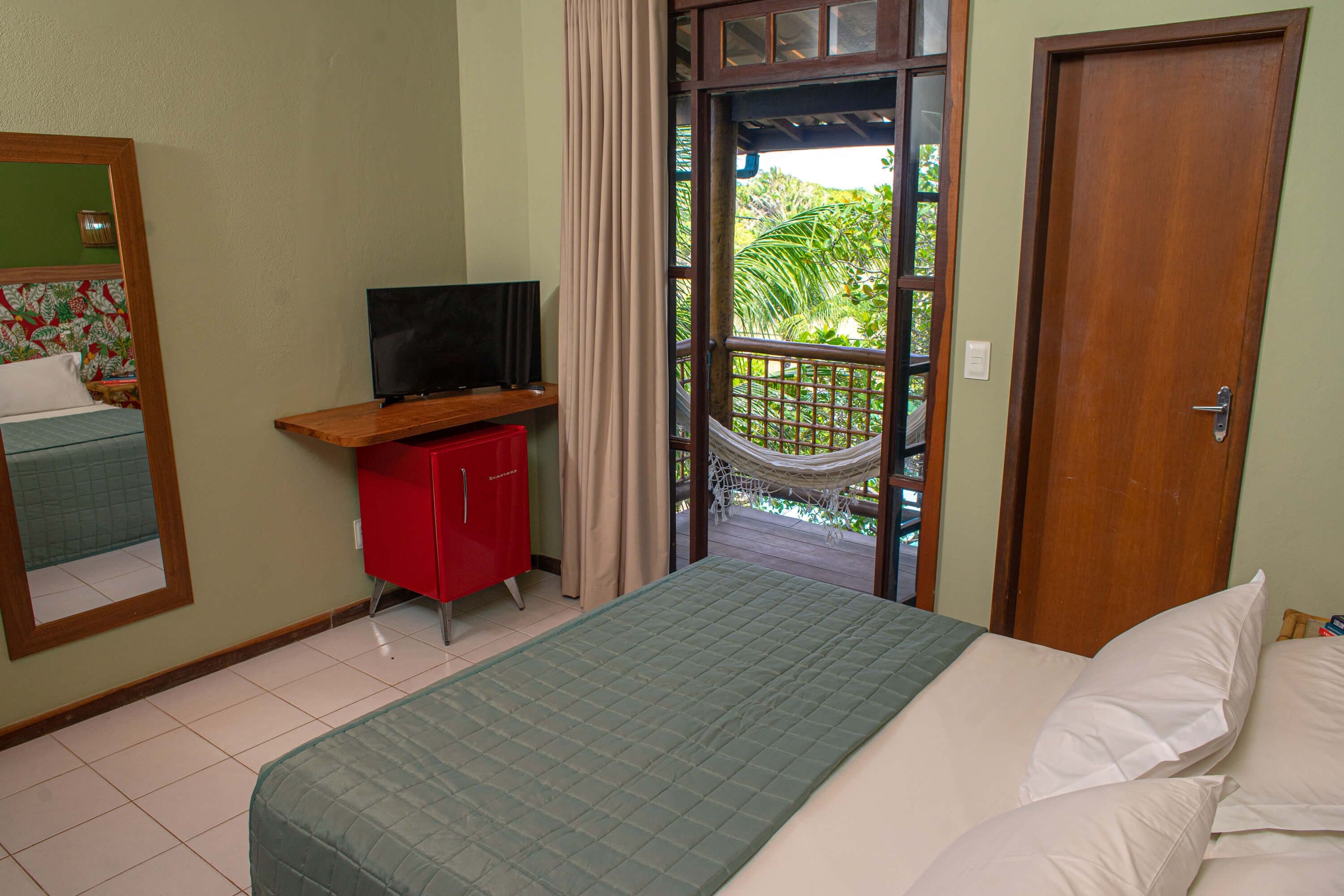 Ein Schlafzimmer mit einem Bett, einem Fernseher, einem roten Schrank und Blick auf einen Balkon mit einer Hängematte.