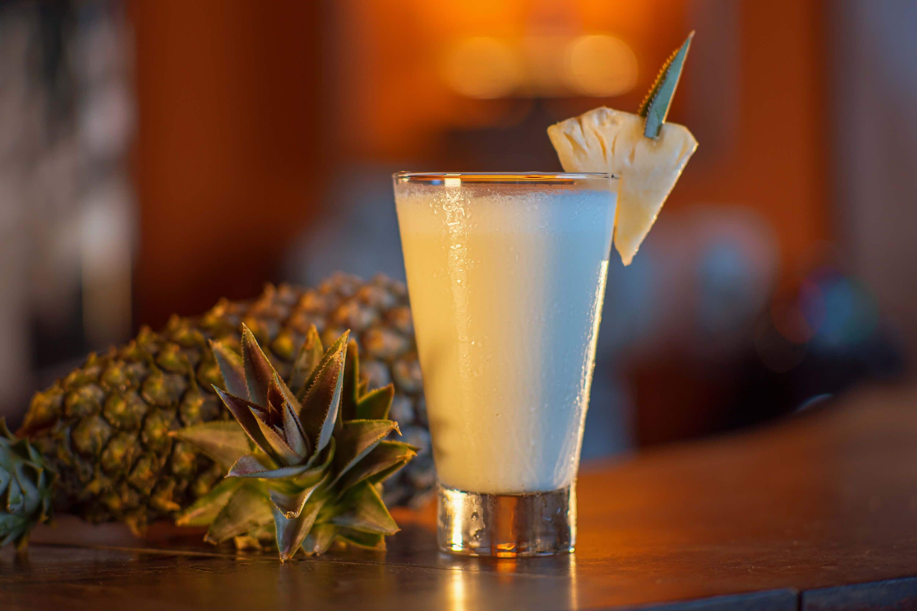 Ein Glas mit einem hellen Getränk und einer Ananas-Garnitur auf einer Bar.