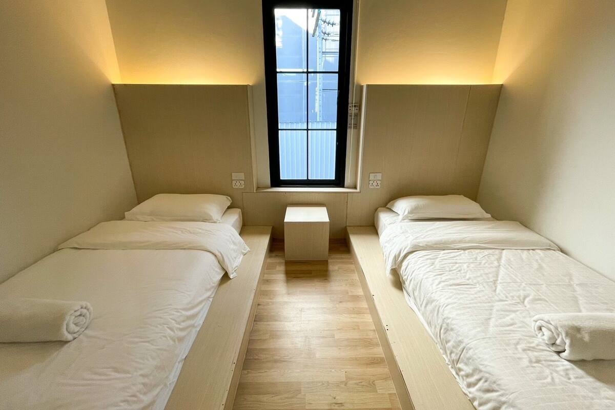 A small, well-lit room with two single beds, a window, and a bench.