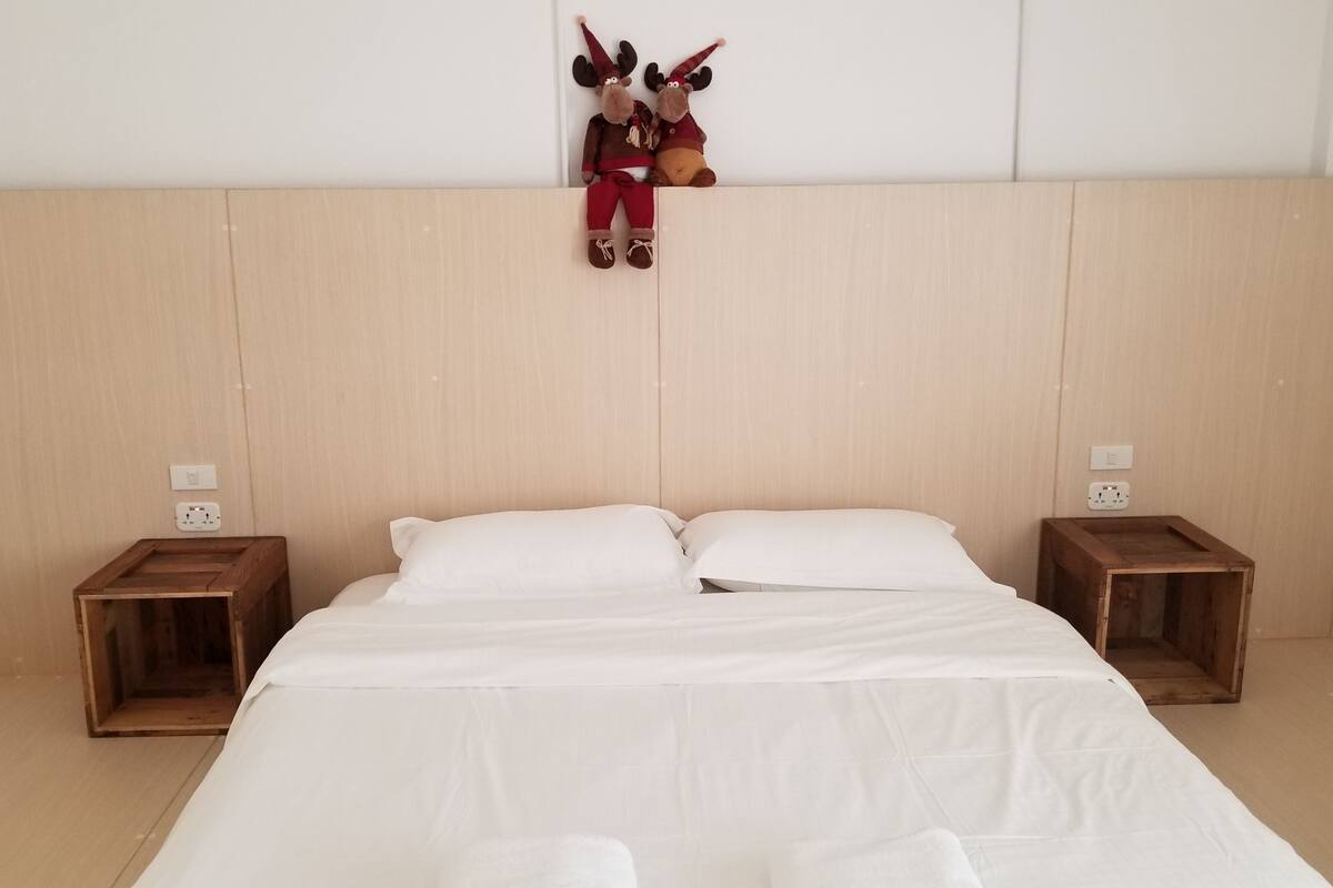 A neatly made bed with white linens, two wooden nightstands, and a wall-mounted decoration of two plush toys.