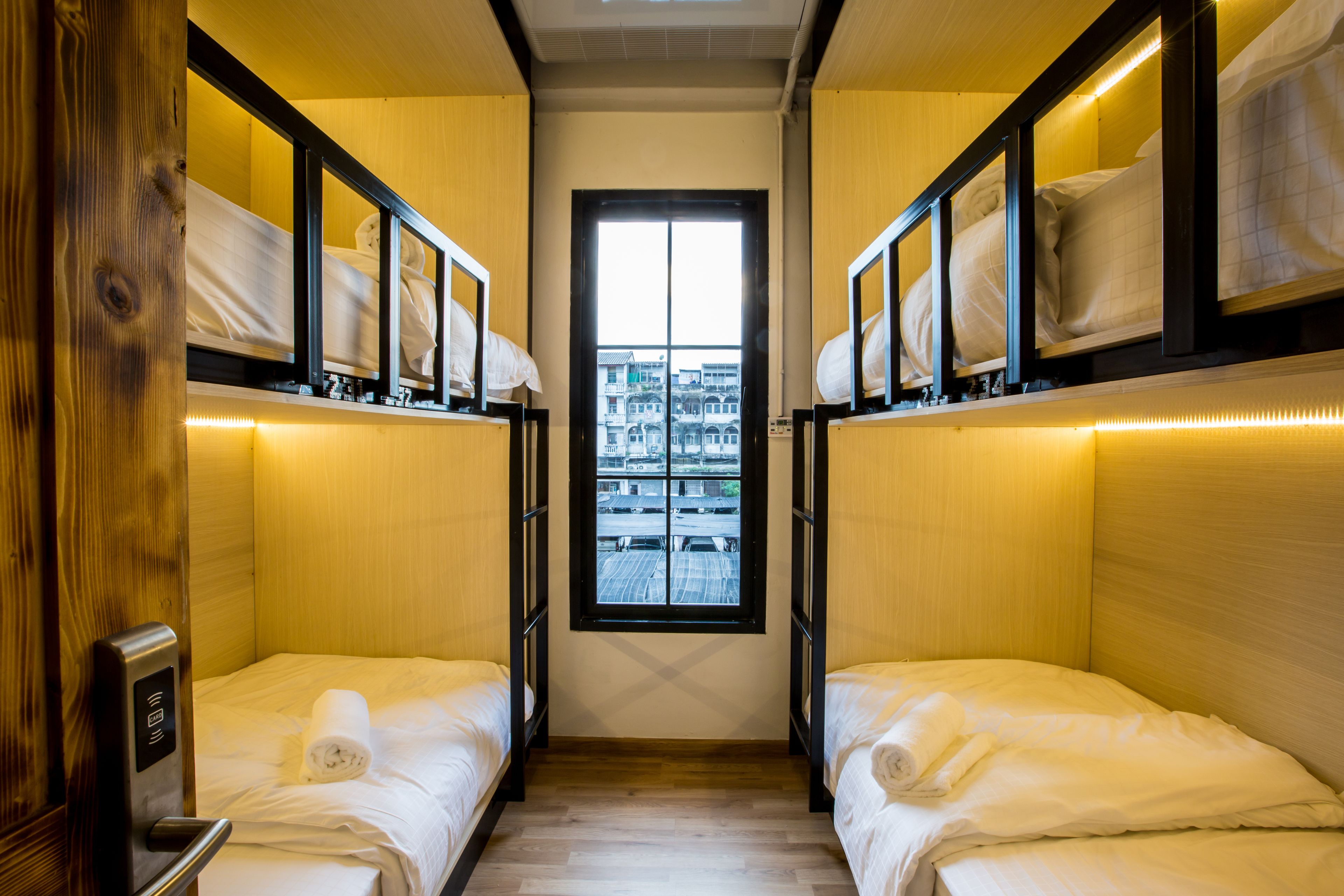 A narrow room with two beds, wooden walls, and a window with a city view.
