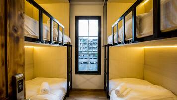 A narrow room with two beds, wooden walls, and a window with a city view.