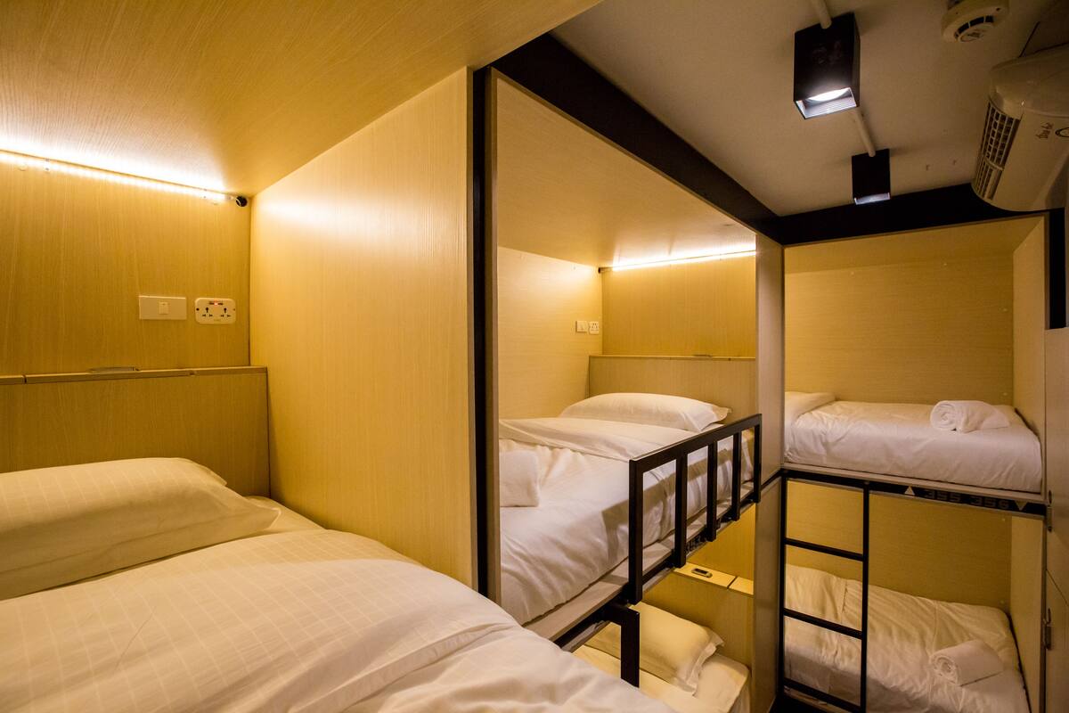 A compact hotel room with bunk beds, a small desk, and a ceiling-mounted projector.