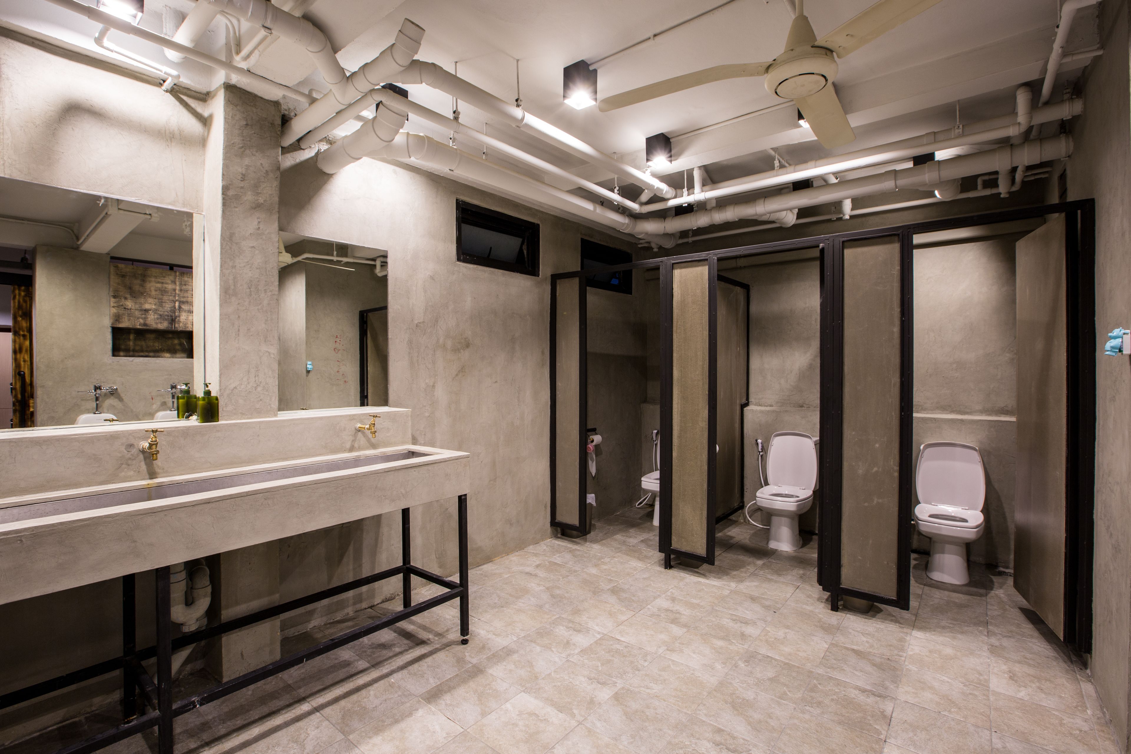 A modern bathroom with a large sink, multiple toilets, and a ceiling fan.