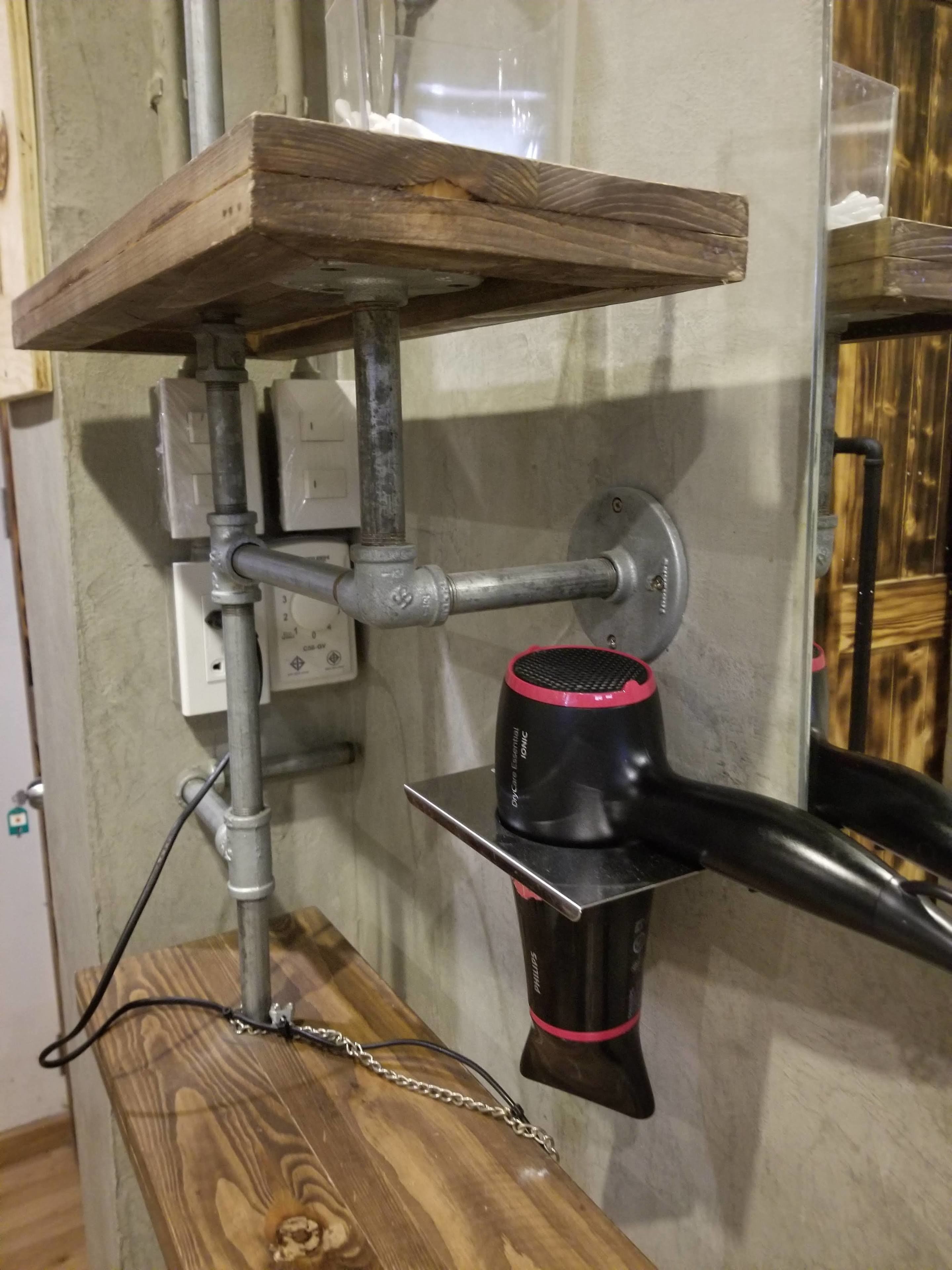 A hairdryer mounted on a wall with a wooden shelf above it.
