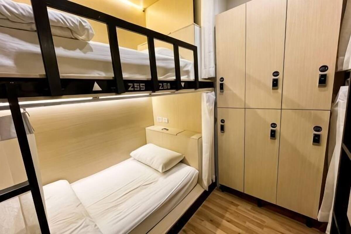 A bunk bed room with a wooden floor, a small bedside table, and a wardrobe with a mirror.