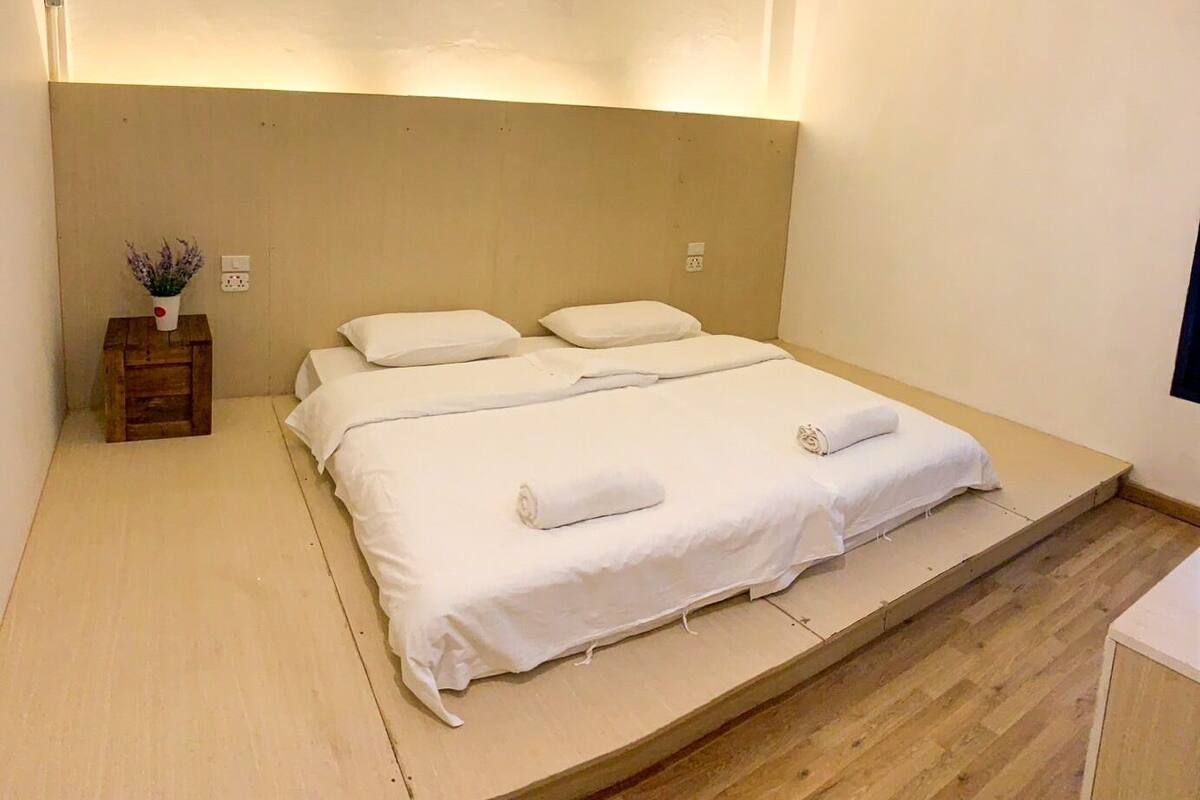A single-bed room with a wooden headboard, white bedding, and a small bedside table with a vase of flowers.