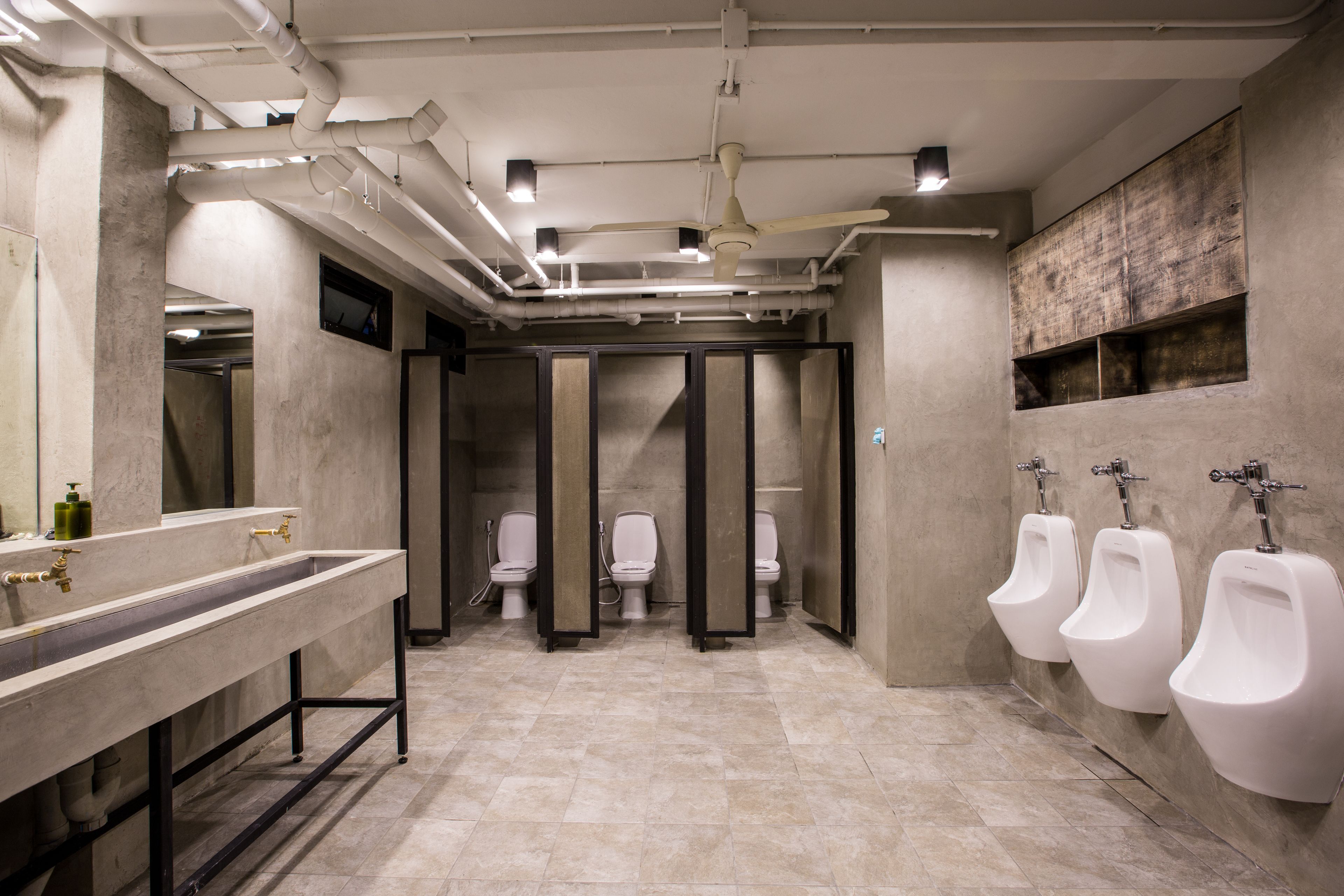 A modern restroom with a long vanity, three urinals, and a ceiling fan.