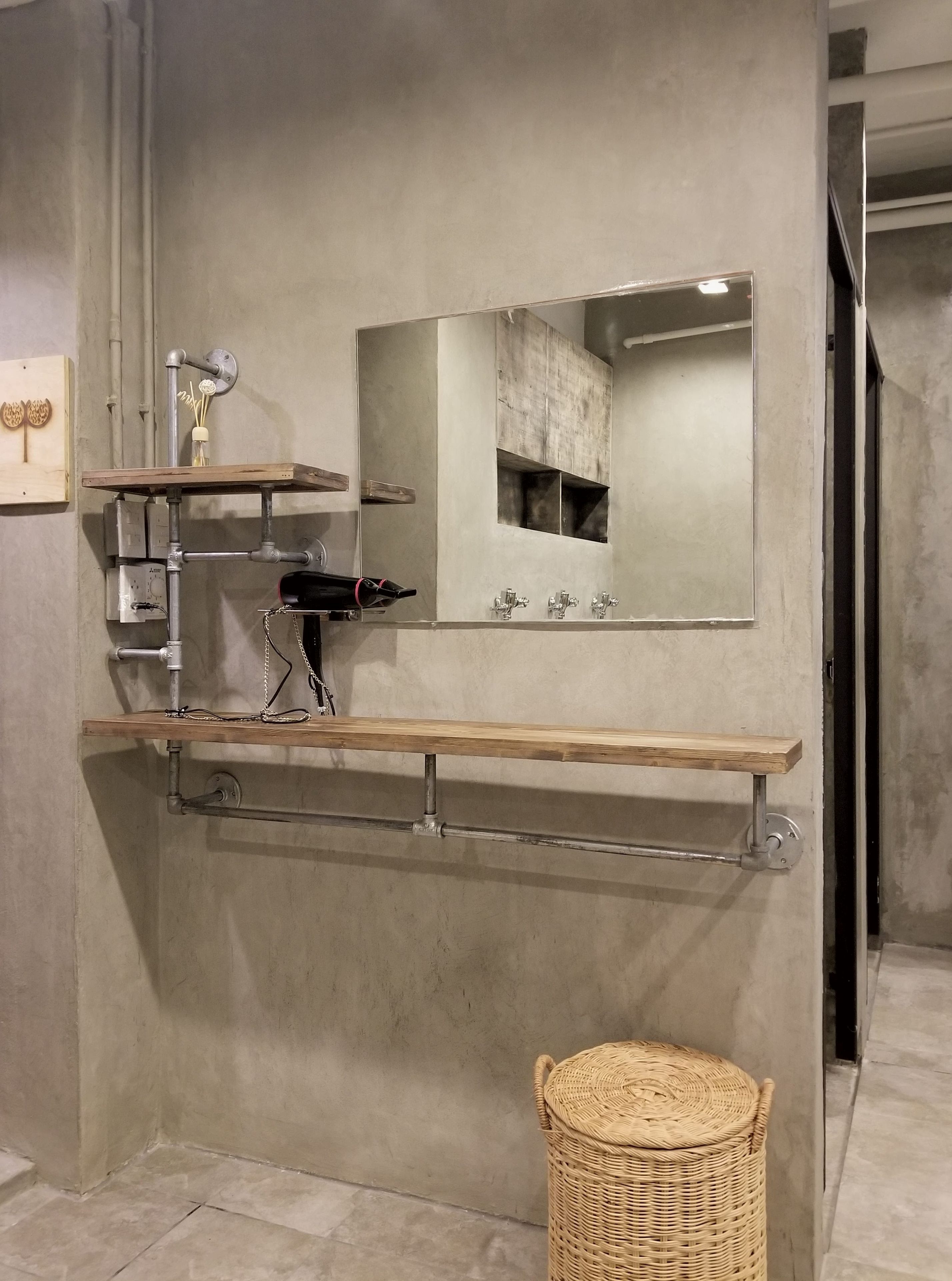 Une salle de bain avec un grand miroir, une étagère en bois, un porte-serviettes et un panier en osier.