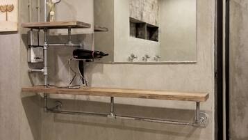 Une salle de bain avec un grand miroir, une étagère en bois, un porte-serviettes et un panier en osier.