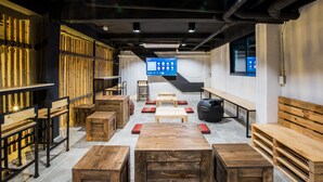 A modern interior with wooden furniture, a large screen, and a bamboo wall. - Bed To Bangkok - Hostel (Bangkok)