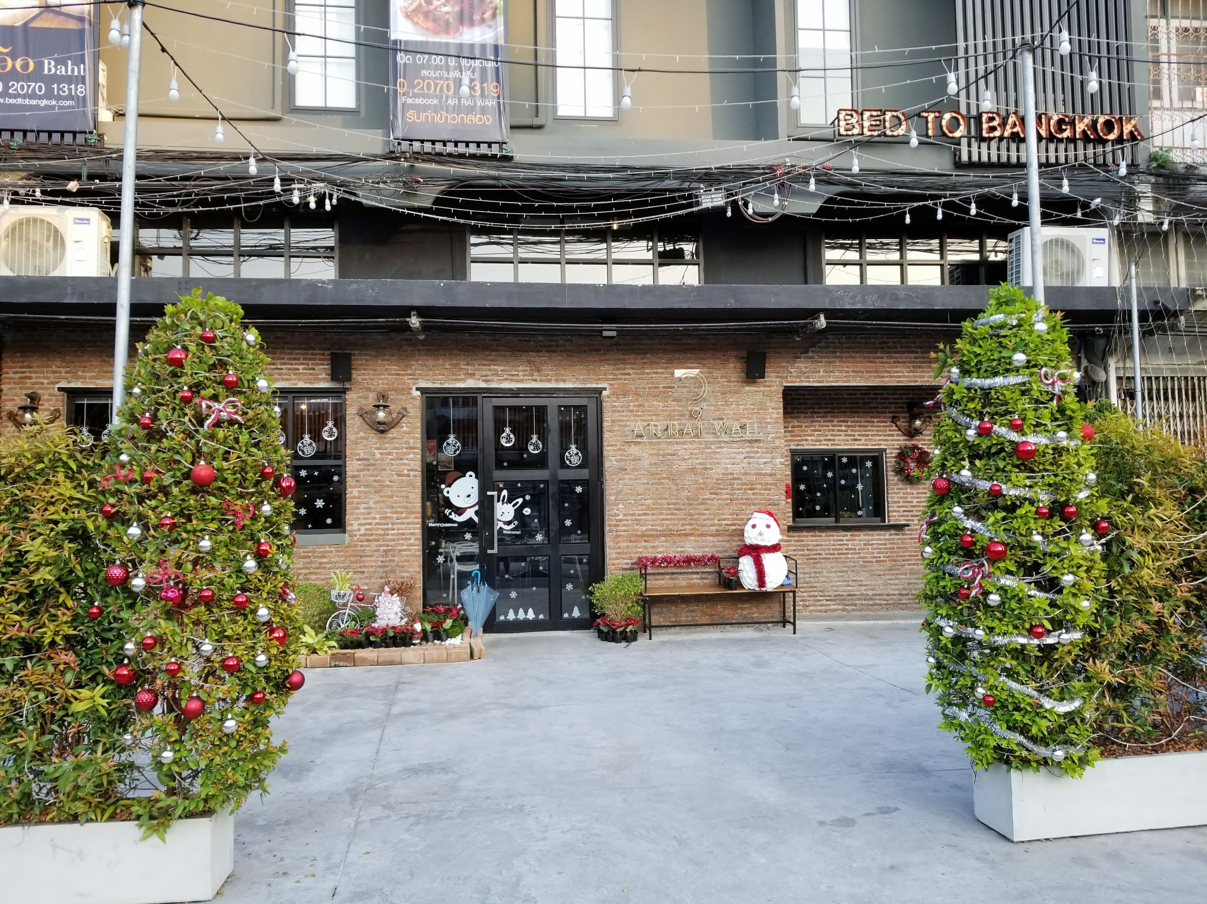 Un bâtiment à la façade en briques, avec une porte noire et des décorations de Noël, notamment deux sapins et un bonhomme de neige.