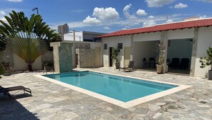 A swimming pool with stone tiles, a palm tree, and a building with a red roof. - Pérola Verde Hotel (Birigui)