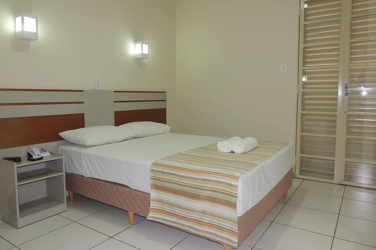 A neatly made bed with a striped blanket, a bedside table with a phone, and a wardrobe with a sliding door.