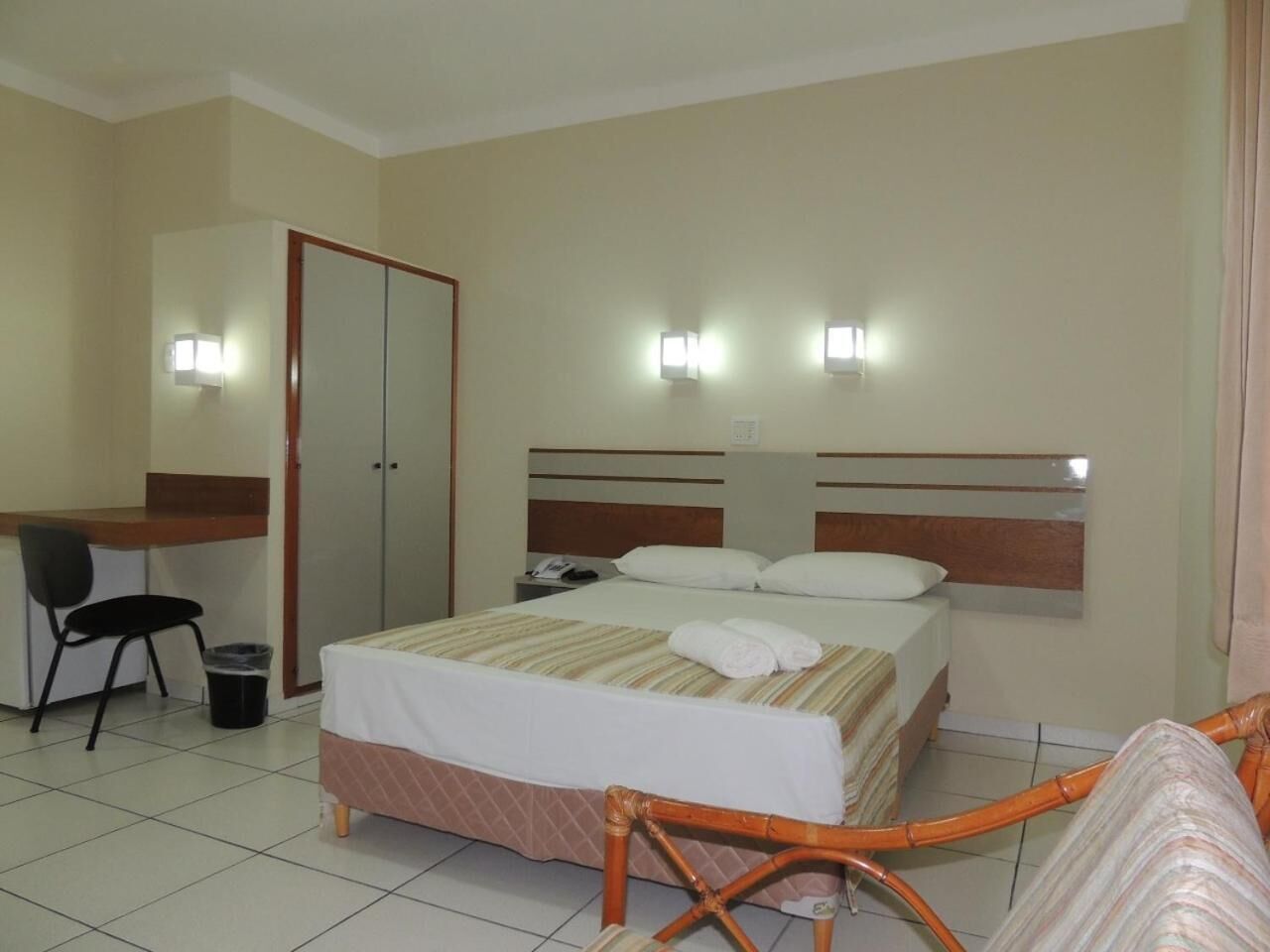 A hotel room with a bed, a desk, a chair, a wardrobe, and a trash bin.
