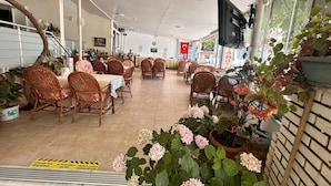 A spacious indoor dining area with wicker chairs and tables, a tiled floor, and potted plants. - Derya Motel (Manavgat)