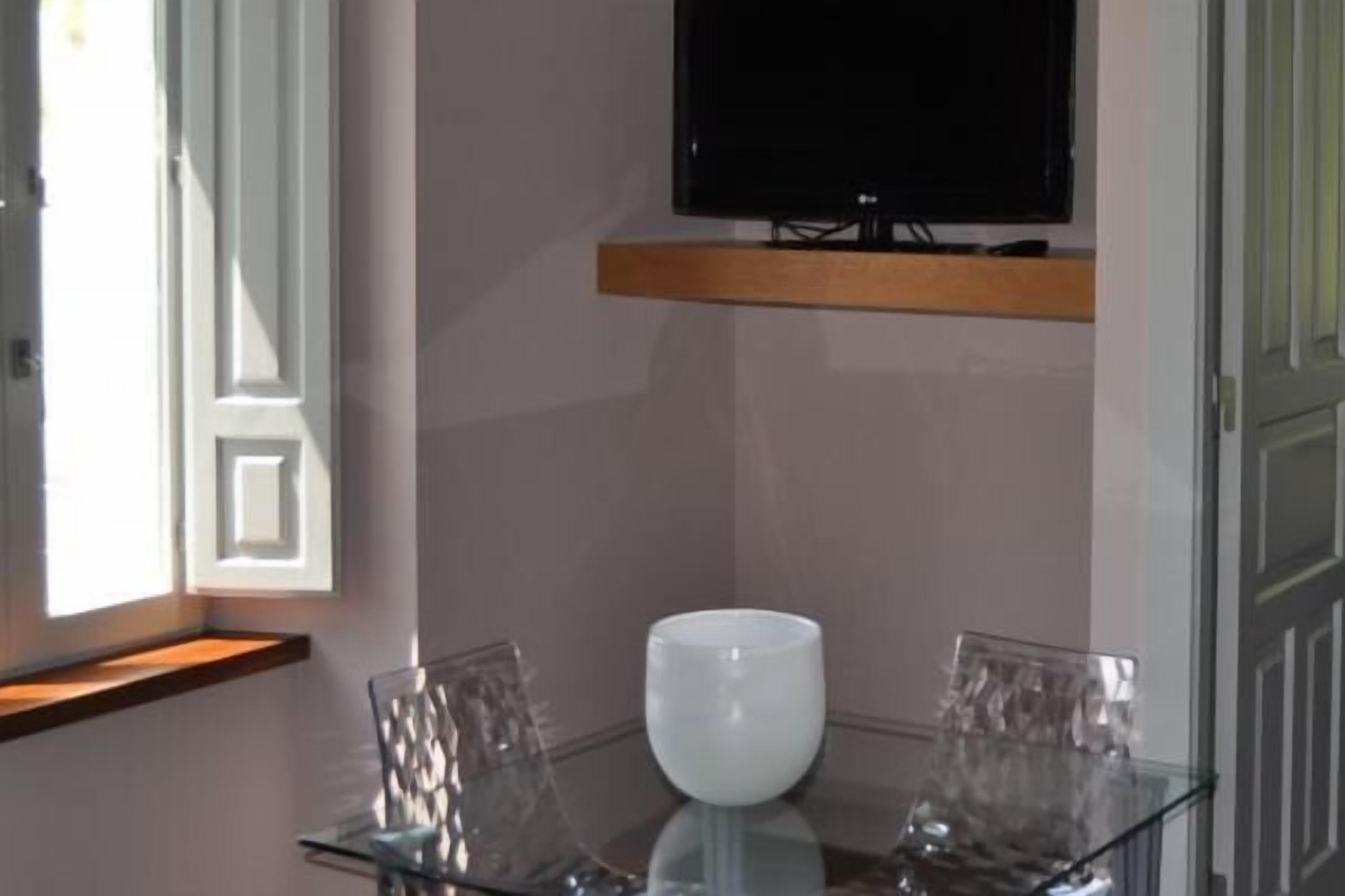 Una habitación moderna con una mesa de vidrio, un florero blanco y un televisor montado.