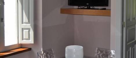 Una habitación moderna con una mesa de vidrio, un florero blanco y un televisor montado.