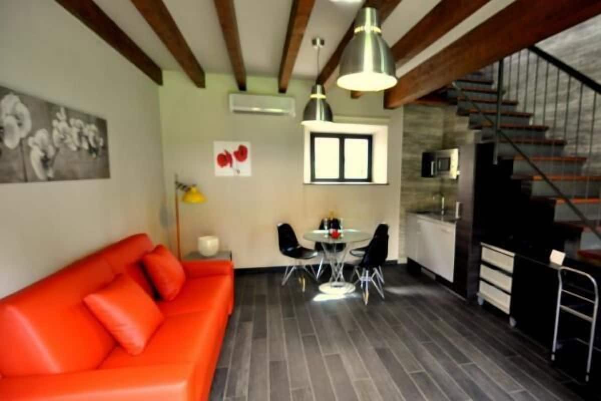 Un espace de vie moderne avec un canapé rouge, un coin repas comprenant une petite table et des chaises, et un escalier menant à un niveau supérieur.