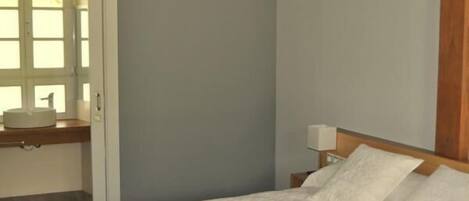A bedroom with a bed, a nightstand, a window, and a sink.