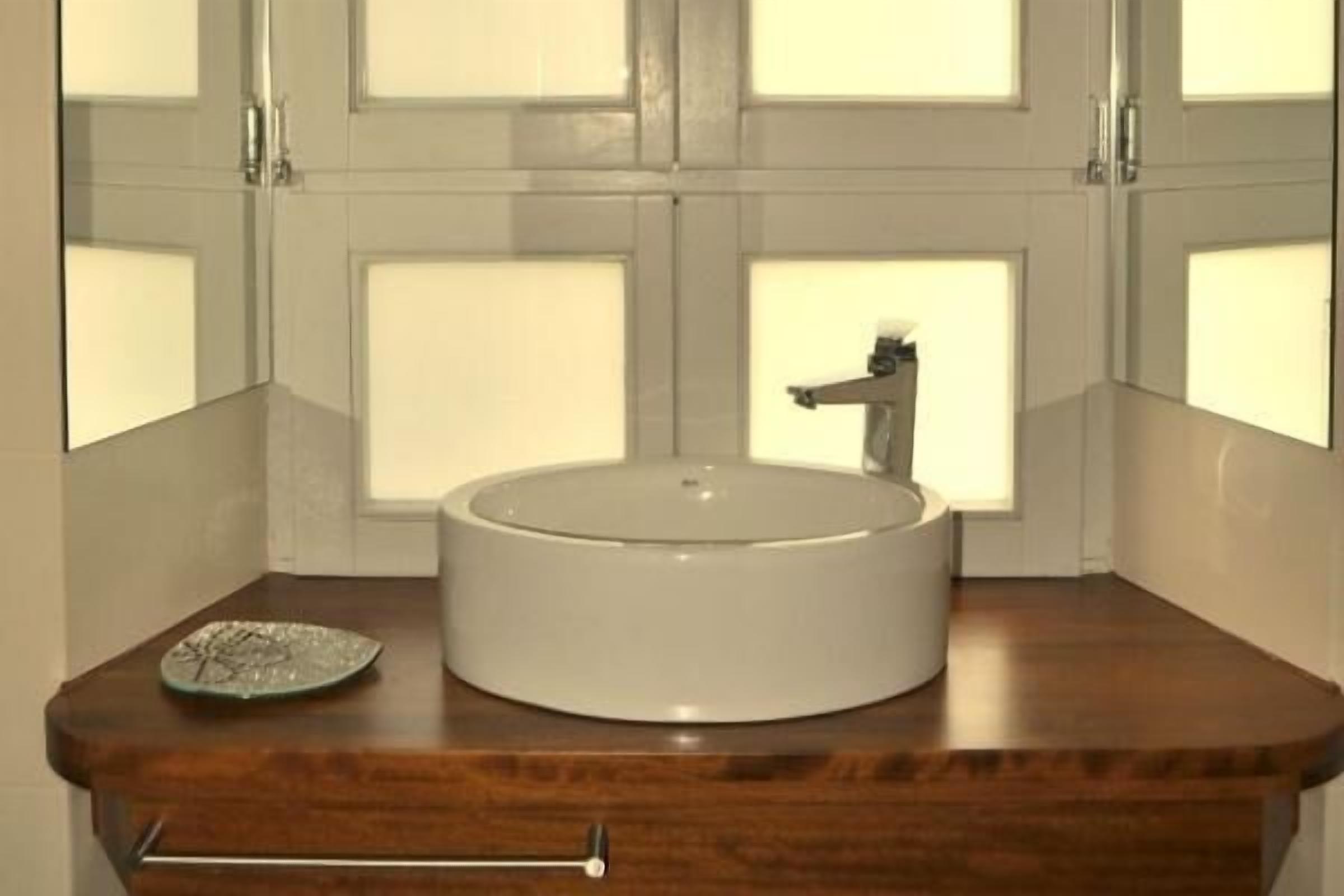 Une salle de bain avec un lavabo rond, un miroir et une fenêtre.
