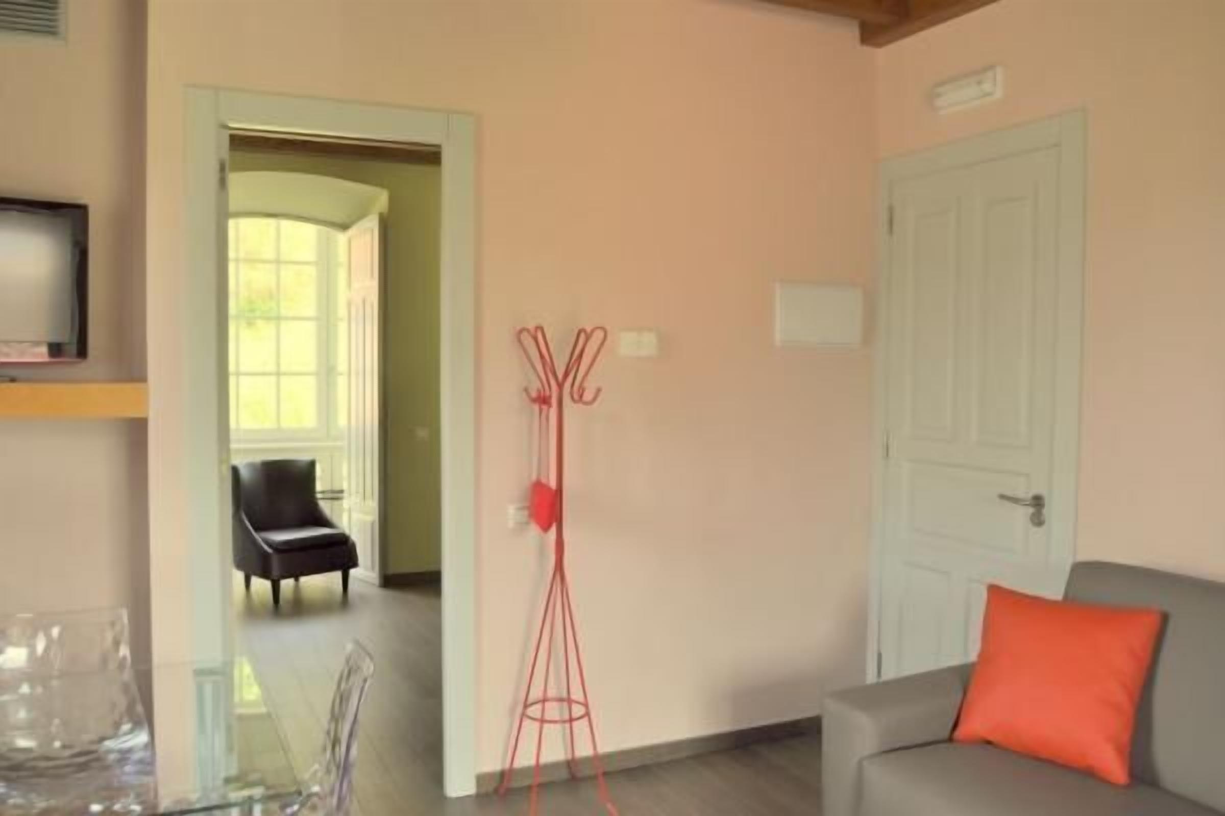 Une pièce avec un canapé gris, un porte-manteau rouge, une porte blanche et une chaise à l’arrière-plan.