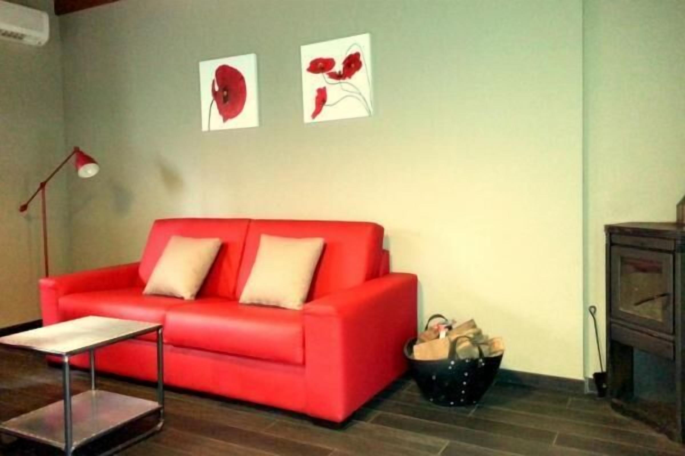 Un sofá rojo con dos cojines, una mesita y una cesta de objetos en el suelo.