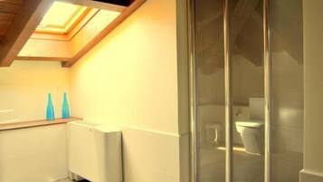 Un baño con tragaluz, cabina de ducha de vidrio y radiador blanco.
