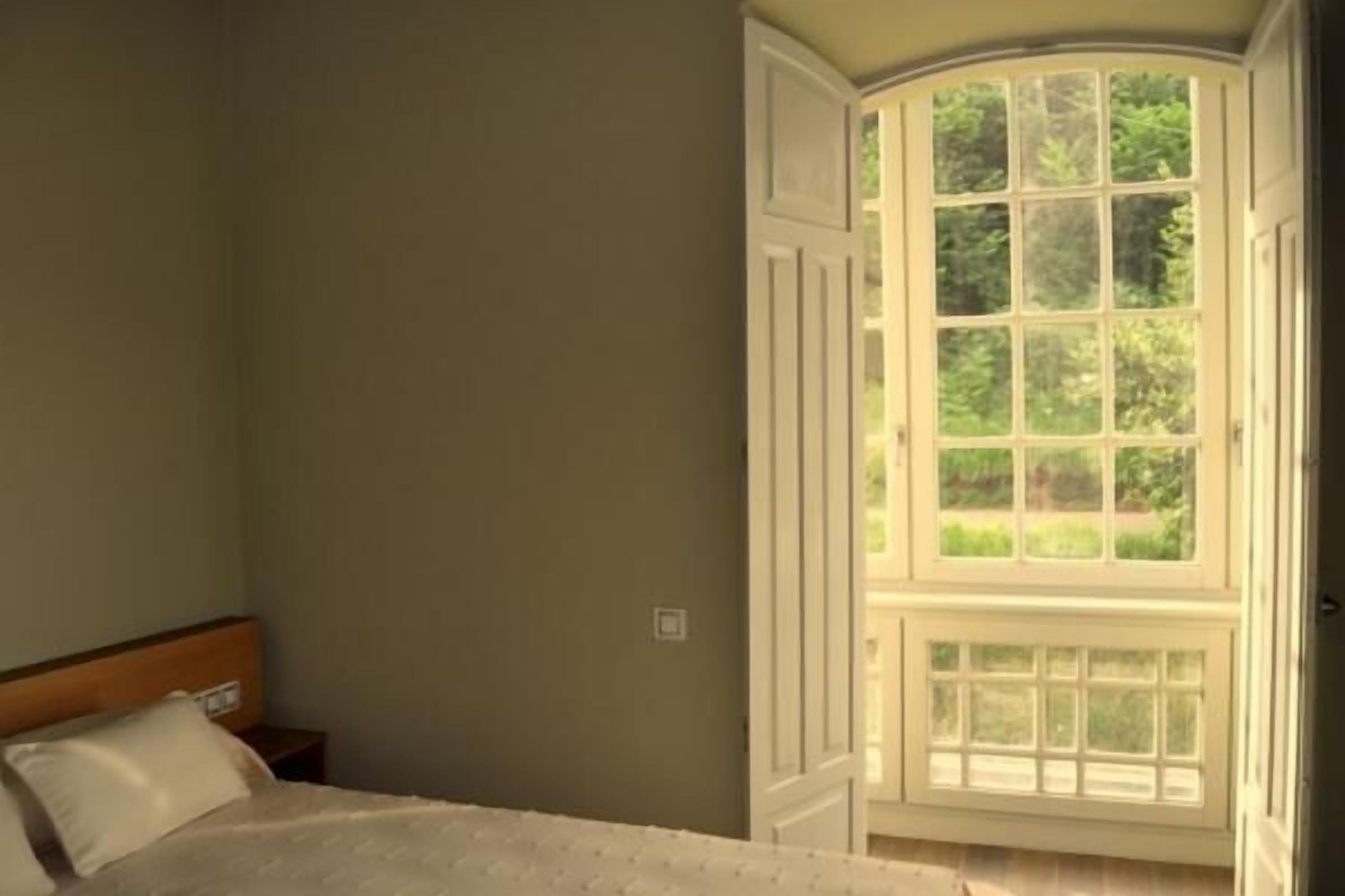 A bedroom with a large bay window, a wooden headboard, and a nightstand.