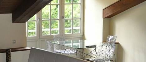Une pièce moderne comprenant un canapé, une table à manger avec des chaises et une grande fenêtre donnant sur un paysage verdoyant.