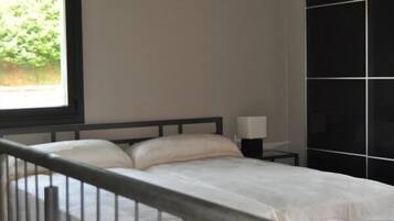 Un dormitorio con cama, mesita de noche, ventana con vistas a vegetación y pared negra con diseño geométrico.